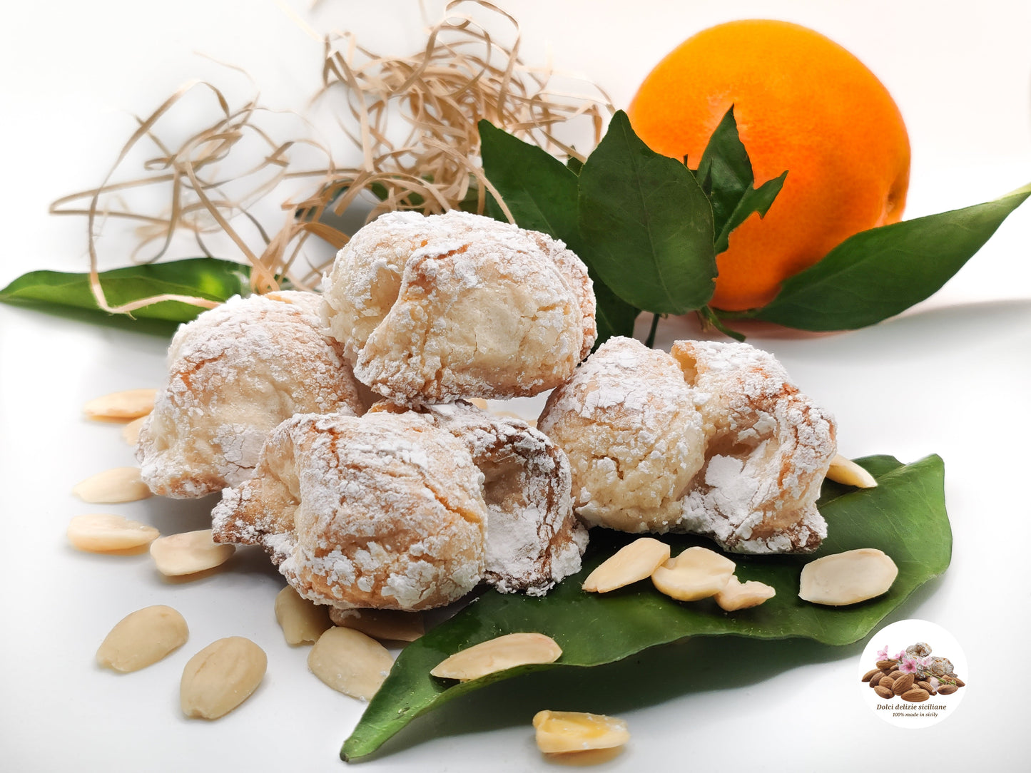 Foto con tre biscotti alle mandorle con zucchero a velo, con sfondo arancia tarocco siciliana e mandorle in petali